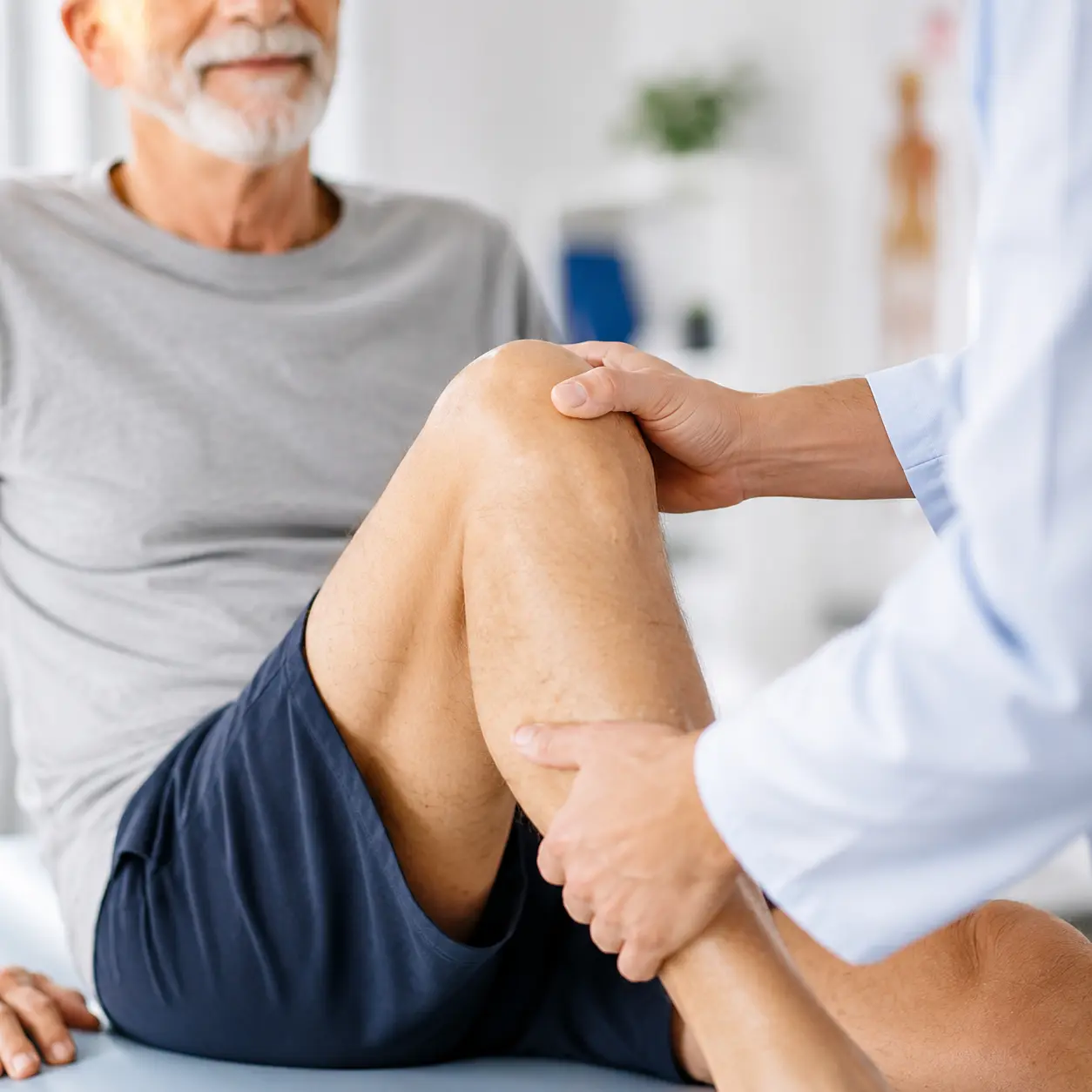 Doctor inspecting a patient's knee on an exam table in a medical office.